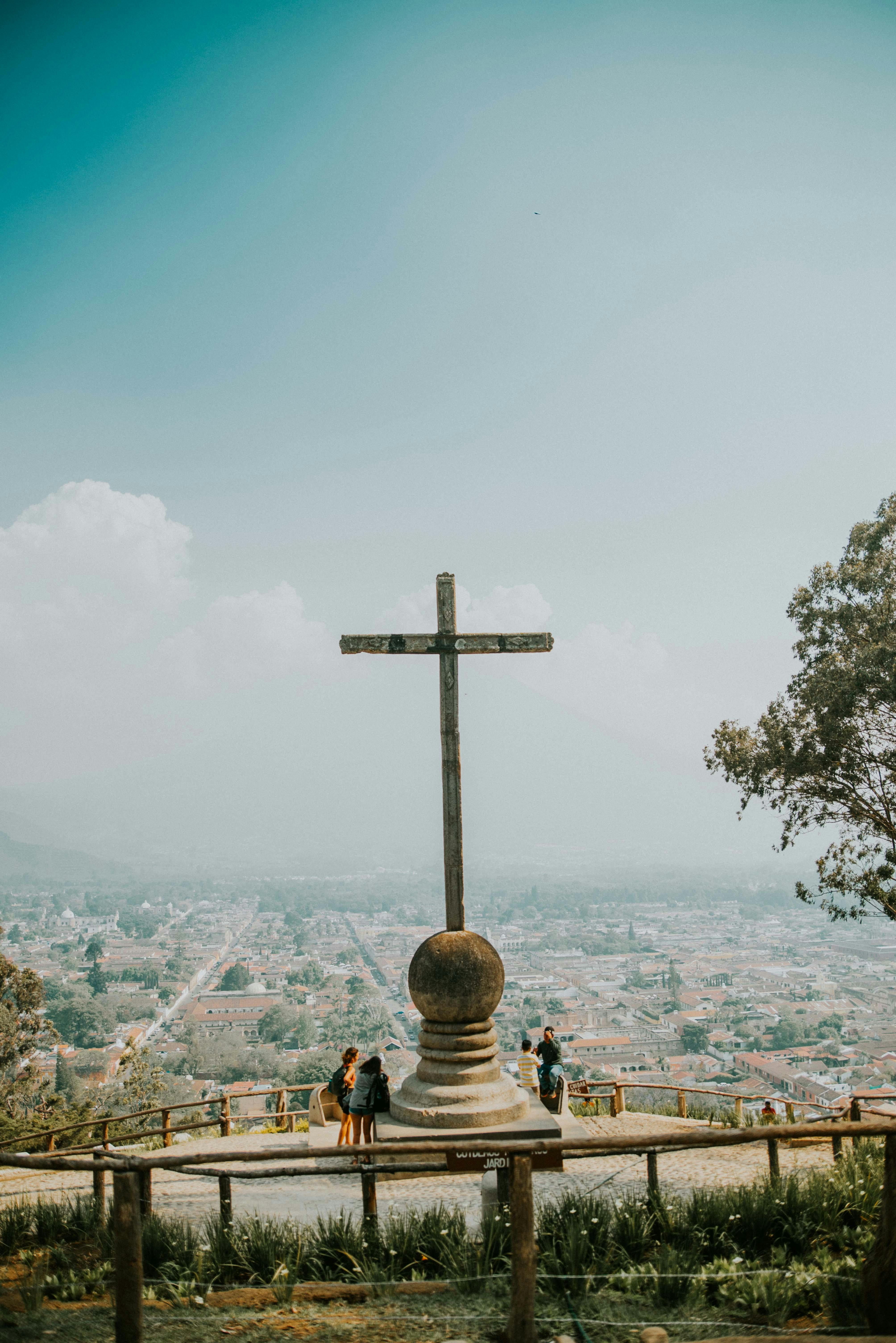 View from the Hill of the Cross overlooking Antigua Guatemala with a cross and people in the foreground.
