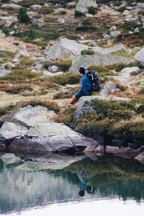 Free A peaceful moment of a hiker sitting on rocks by a serene lake in Barèges, France. Stock Photo