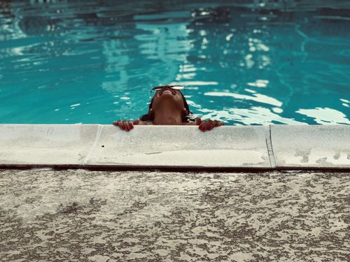 Free Woman smiling while relaxing in a turquoise swimming pool, perfect for summer leisure. Stock Photo