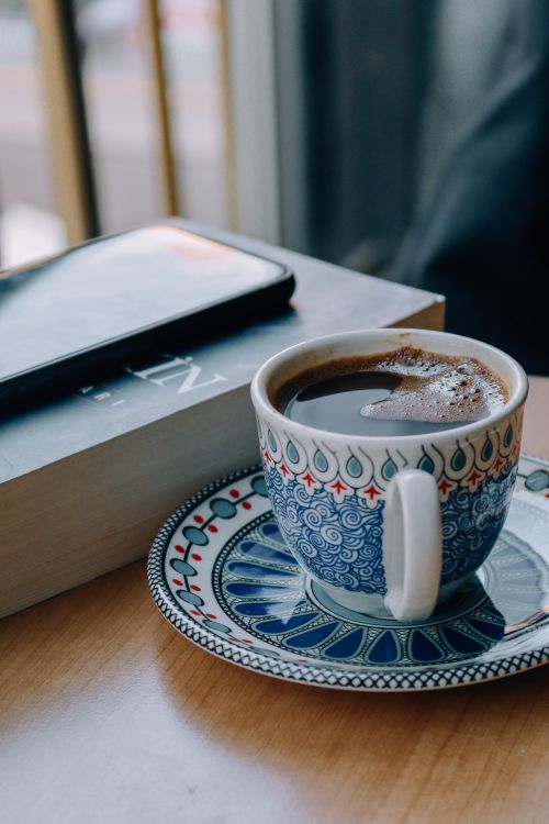 Free Enjoy a serene coffee break with a traditional cup, book, and smartphone in a cozy café setting. Stock Photo