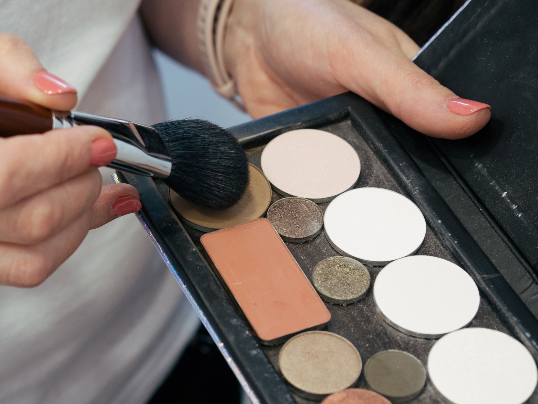 Female hands holding a makeup brush and palette for cosmetic application.