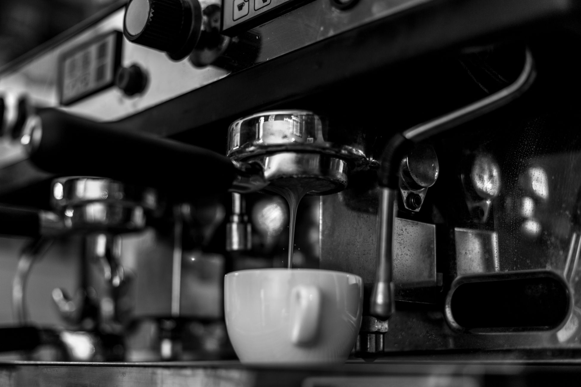 Black and white close-up of an espresso machine preparing coffee into a cup, highlighting the brewing process.