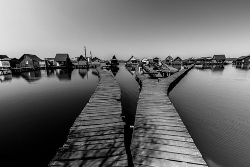 Free Black and white capture of Bokod's scenic boardwalk and floating cottages on a calm lake. Stock Photo