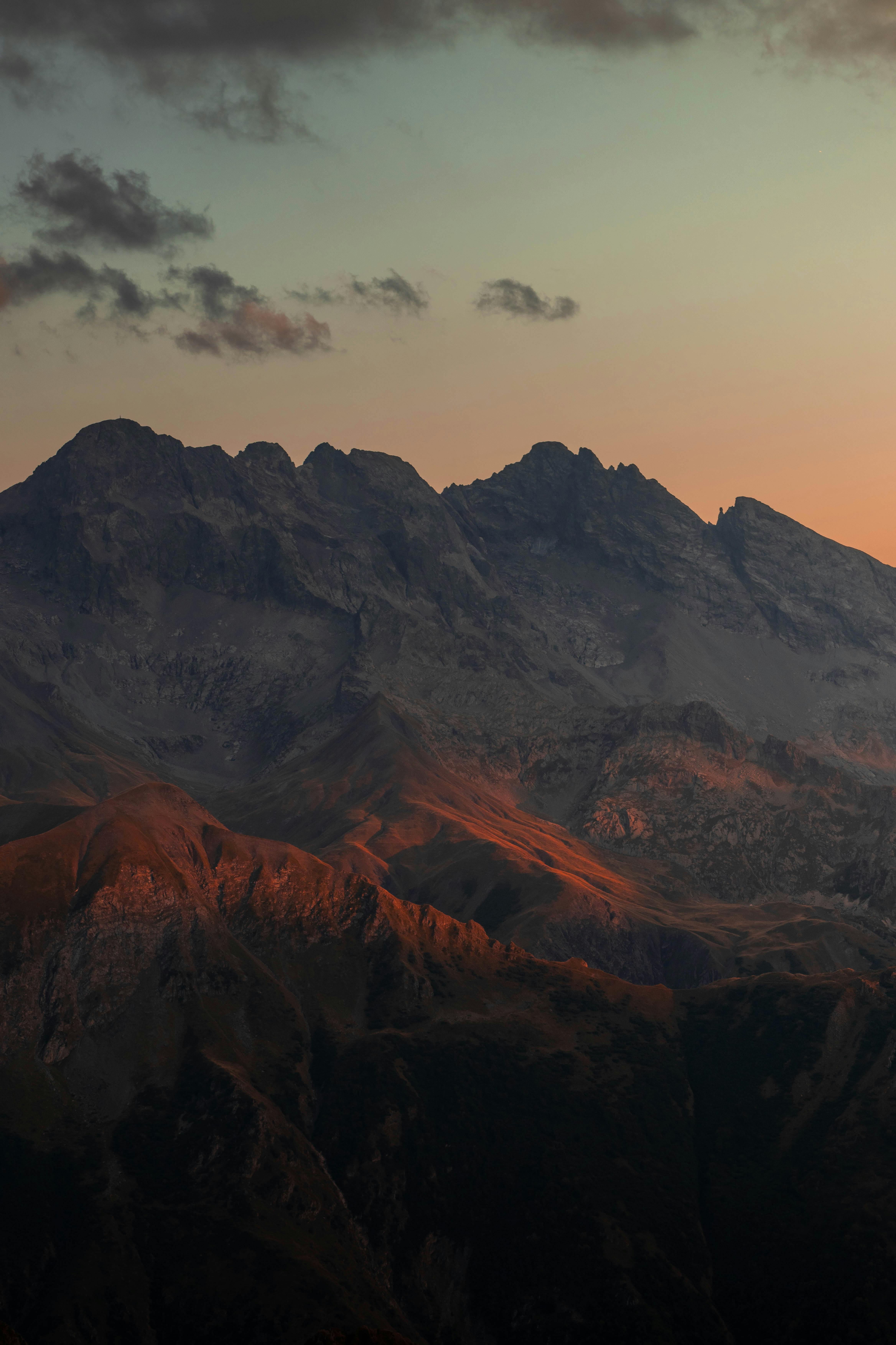 Dramatic landscape of mountain peaks during sunrise with warm light casting over rocky terrain.