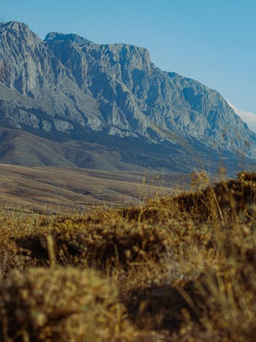 Free Breathtaking view of a rugged mountain range with clear blue skies and dry grassland. Stock Photo