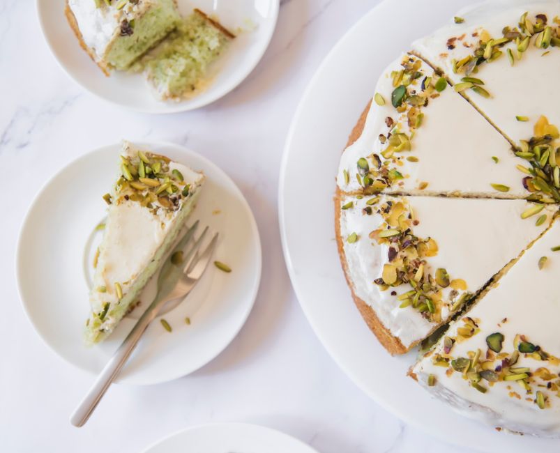 Top view of sliced pistachio cake with cream topping on a white plate for dessert.