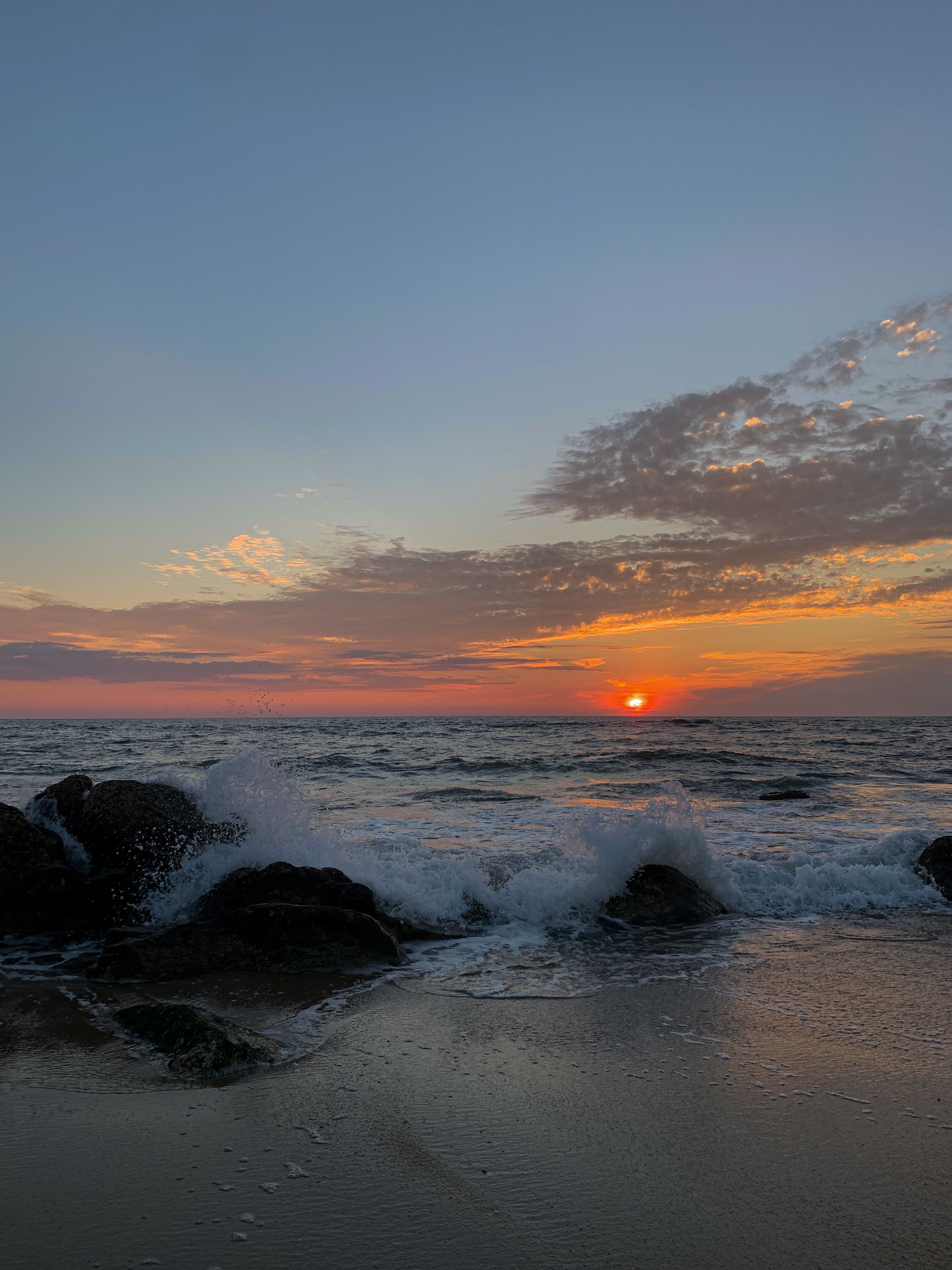 Captivating sunset view with waves crashing over rocks by the serene ocean shore.
