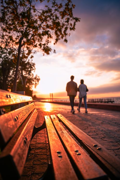 Free Couple walking along a scenic waterfront path at sunset, embracing a serene moment. Stock Photo