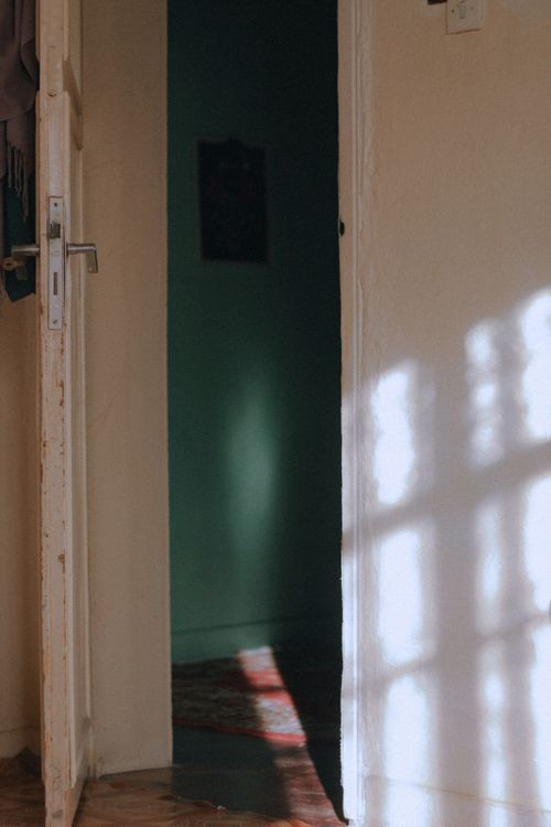 Free A partially open door with sunlight casting intricate shadows on a wall in a serene interior setting. Stock Photo