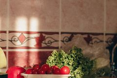 Close-up of fresh vegetables on a kitchen counter with natural light highlighting tomatoes and greens.