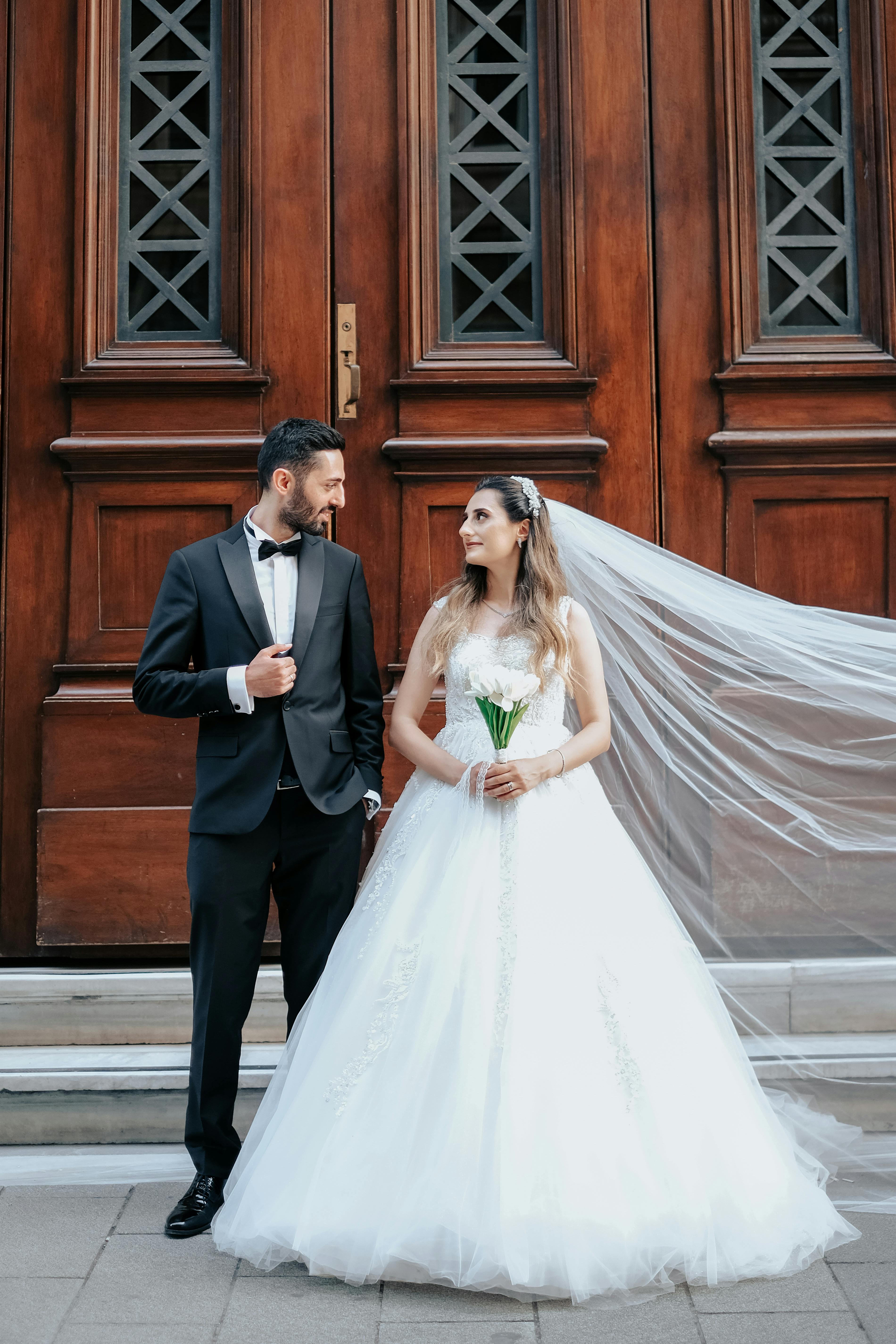 Man in Black Suit and Woman in White Wedding Dress Holding Hands Facing ...