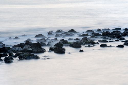 Free Serene view of waves gently washing over rocky shoreline, creating a misty effect. Stock Photo