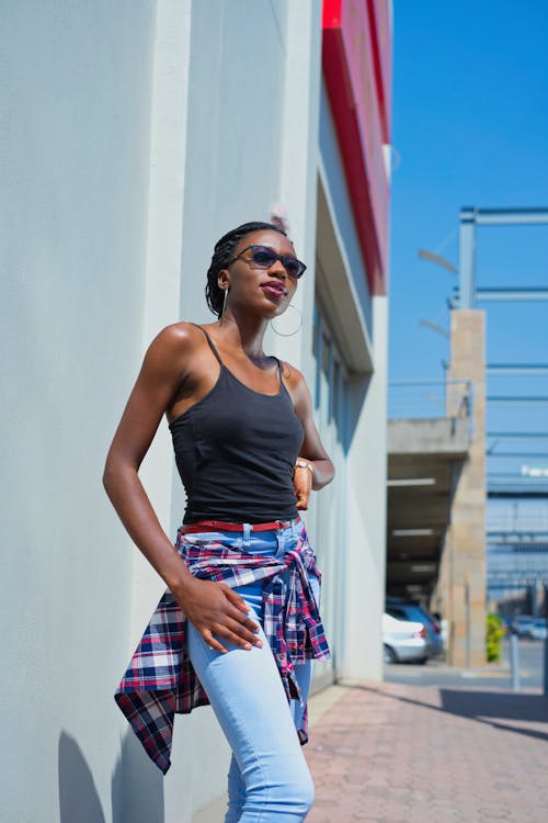 A Woman in Black Tank Top Wearing Sunglasses while Standing on the Street