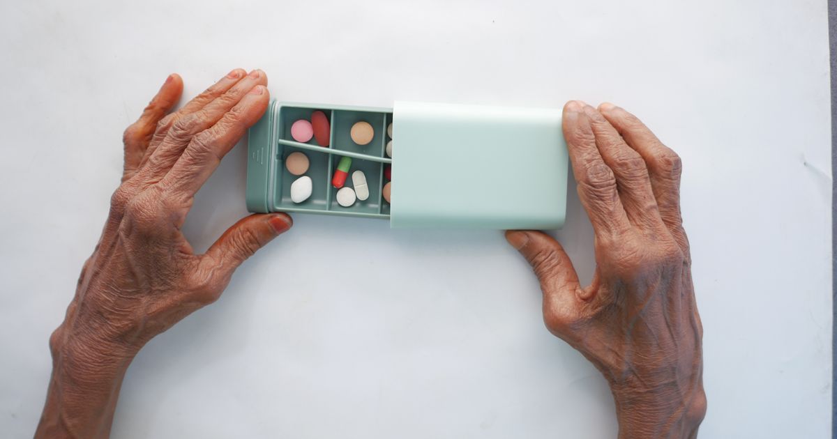 Elderly hands opening a weekly pill organizer containing several medications