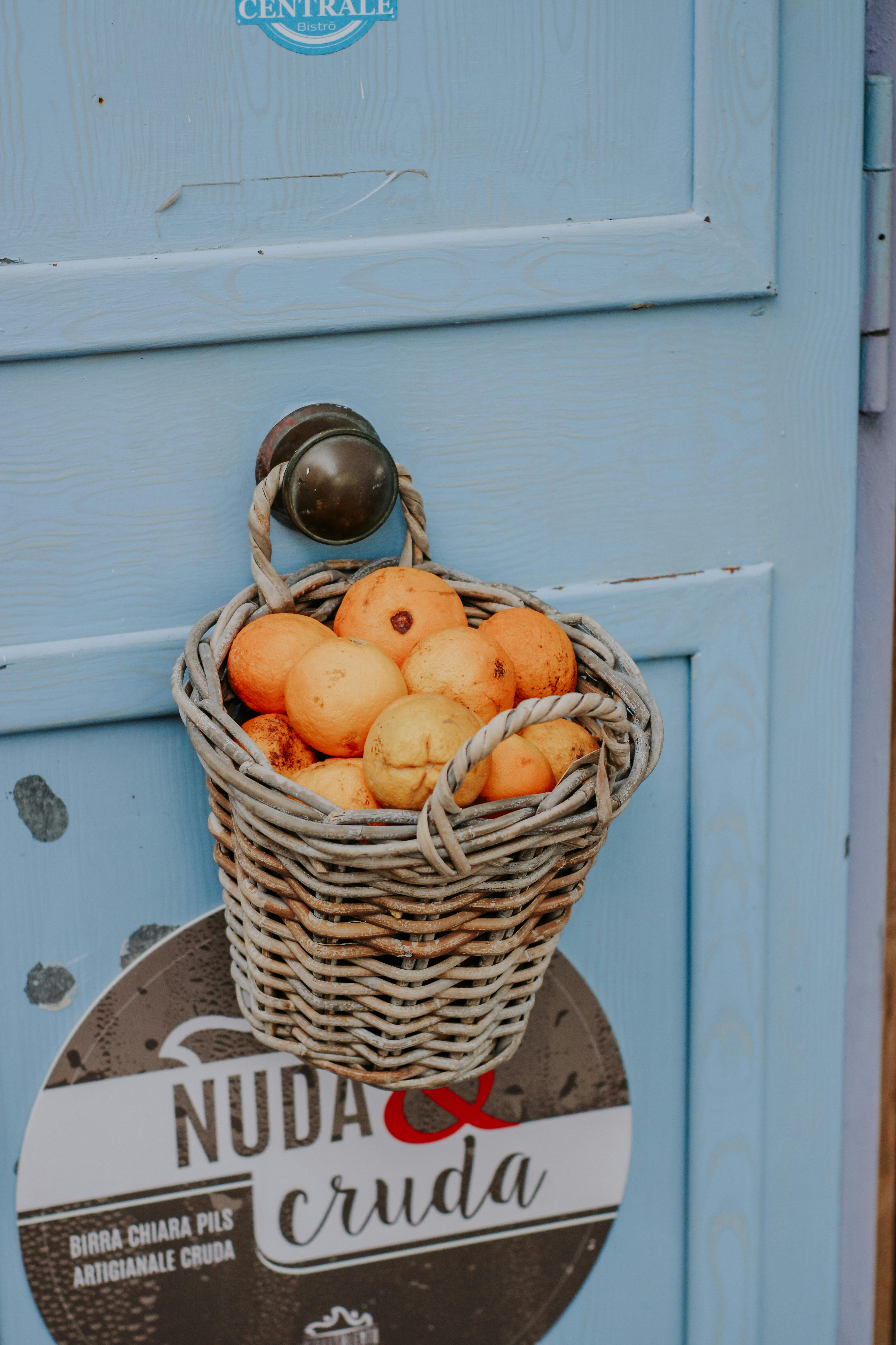 Rustic basket filled with oranges hanging on a blue door with vintage sign.