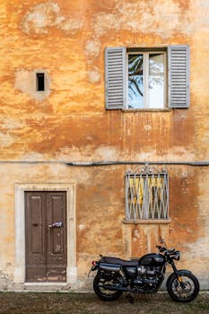 A classic motorcycle parked by a weathered wall in Urbino, Italy, showcasing timeless architecture.