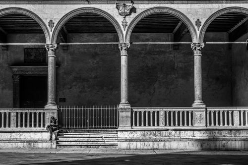 Free Black and white photo of a woman sitting by historic arches in Verona, Italy. Stock Photo