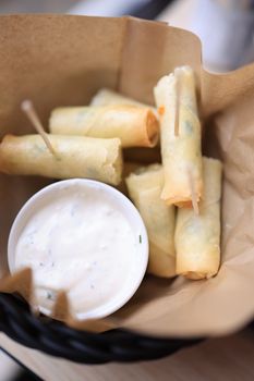 Close-up of crispy spring rolls served with a creamy dipping sauce, perfectly arranged in a paper wrap.