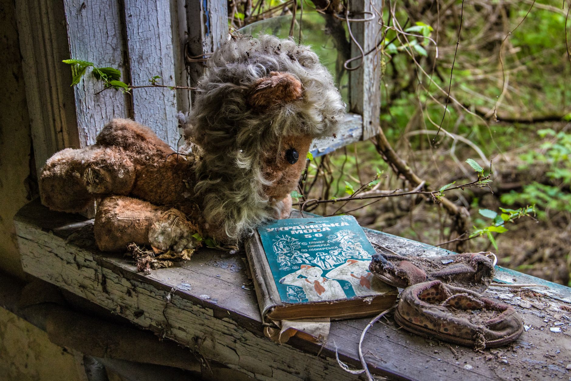 Eerie scene of a worn-out stuffed toy and book in an abandoned Chernobyl window.