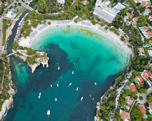 Free Stunning aerial shot of Cala Galdana with turquoise waters, boats, and lush greenery. Stock Photo