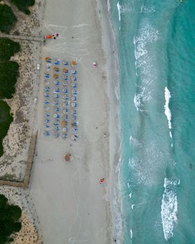 Drone shot of Sant Tomas Beach, Menorca with sun loungers and turquoise waves.