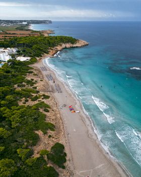 Explore the breathtaking aerial view of Sant Tomàs Beach in Spain with vibrant blue waters and lush greenery.