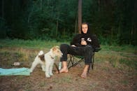 一名男子带着狗，在森林的露营椅上放松身心，享受户外活动