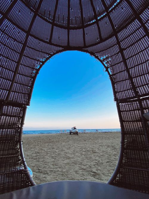 Free A beautiful beach view framed by an arching wicker structure under a clear blue sky. Stock Photo