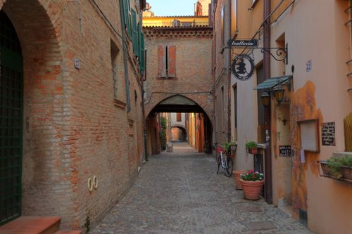 Free Explore a serene cobblestone alley in Ferrara, Emilia-Romagna, lined with historic brick buildings and a trattoria. Stock Photo
