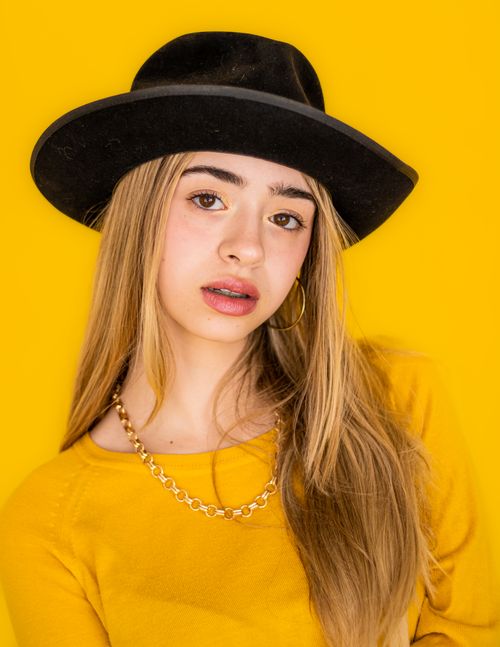 Free Stylish young woman in a black hat and yellow top, showcasing a trendy look against a matching background. Stock Photo