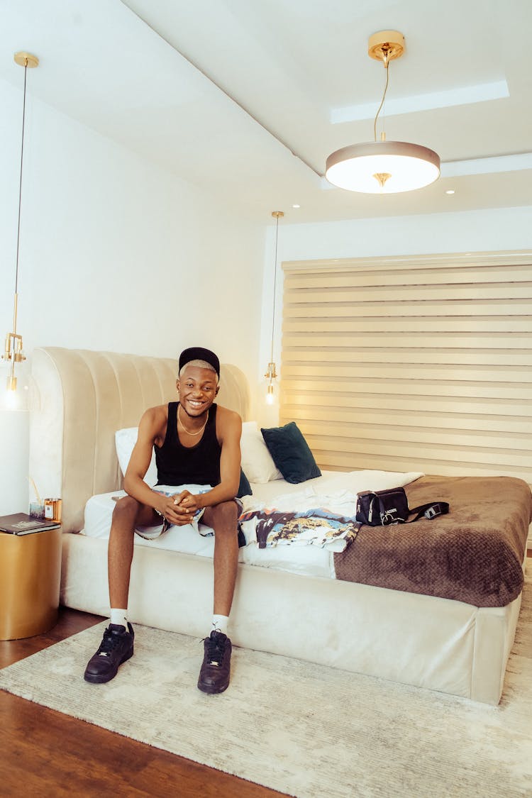 Smiling Man Sitting On Bed In Bedroom