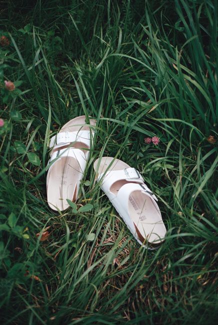 A pair of white sandals resting on vibrant green grass outdoors, evoking summer vibes.