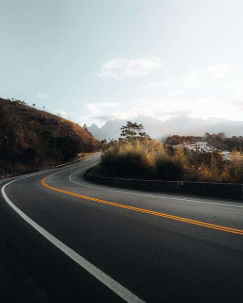 Free Curved road in scenic mountain landscape with bright sky and lush greenery, perfect for travel themes. Stock Photo