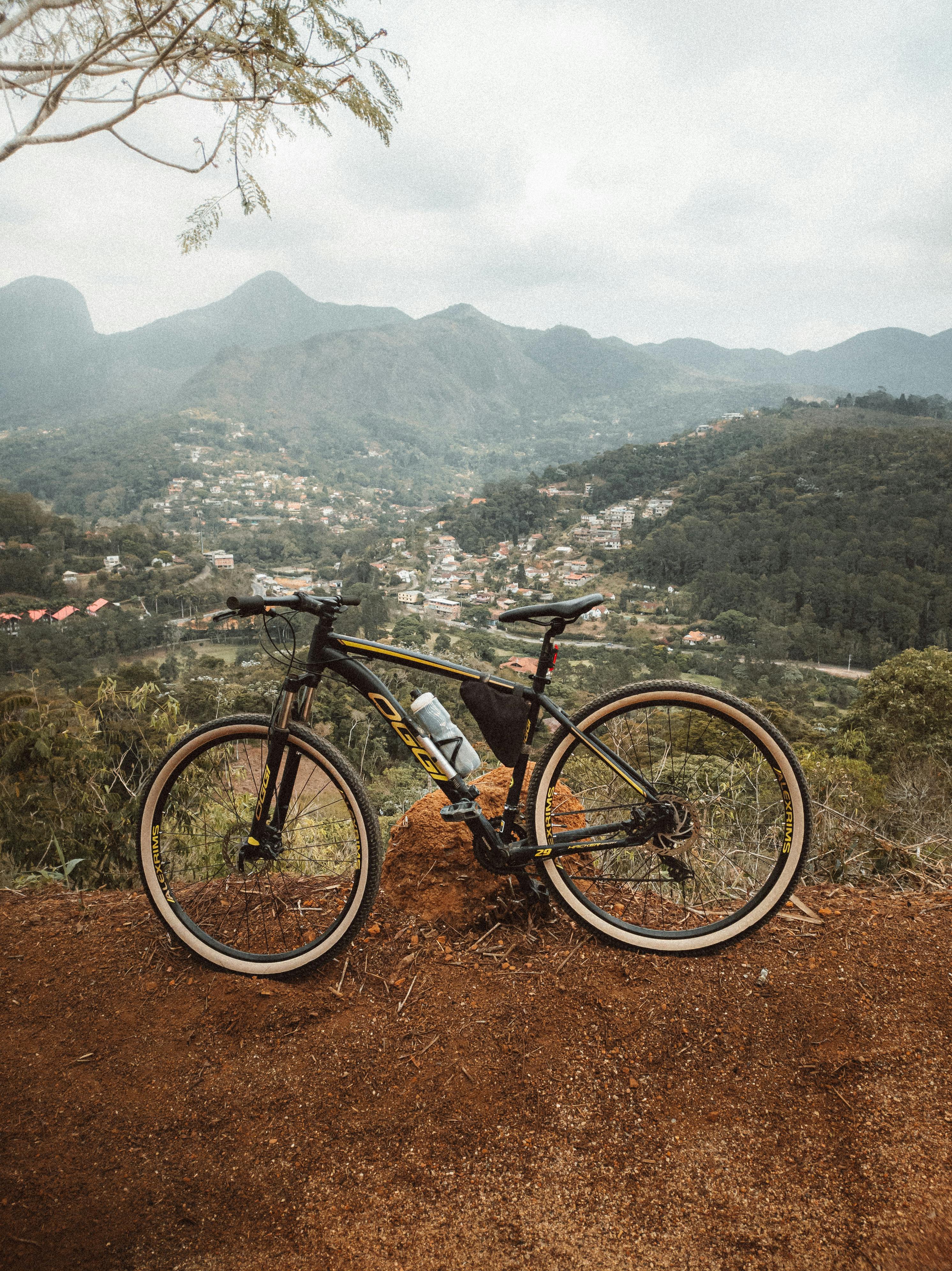 Mountain bike resting on a trail with a scenic overlook of hills and a village below.