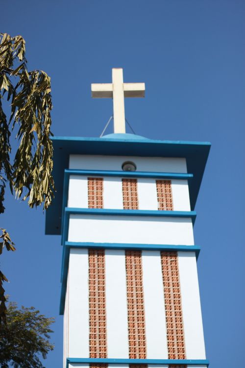 Free Vertical view of a church tower with a prominent white cross against a clear blue sky. Stock Photo