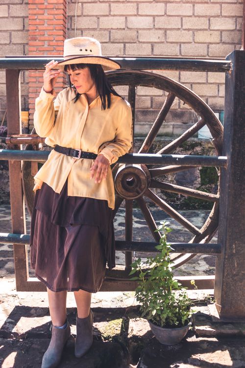 Free A fashionable woman in cowboy attire posing by a rustic wheel fence outdoors. Stock Photo