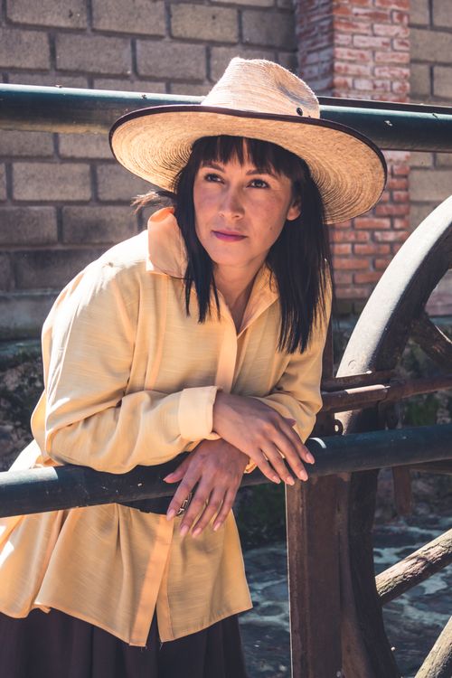 Free Casual woman wearing straw hat and leaning on vintage wheel outdoors. Stock Photo