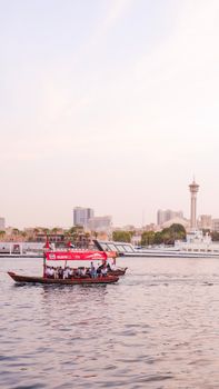 Scenic view of a traditional boat on Dubai Creek with city skyline at sunset.