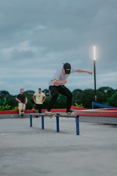 Skateboarder performs a grinding trick on a rail at an outdoor skatepark with onlookers.