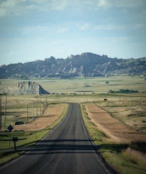 A picturesque open road stretches through vast rural plains with mountains in the distance.