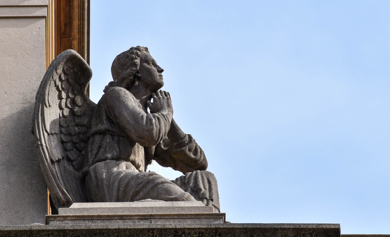 a detailed stone angel sculpture seated in contemplation against a cle