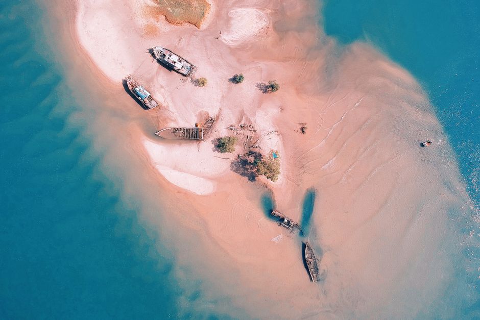 A stunning aerial shot of sunken ships on a sandy beach with clear blue waters.