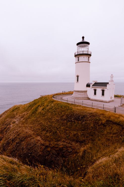 Free A picturesque lighthouse stands watch over a calm, overcast sea, surrounded by grassy cliffs. Stock Photo