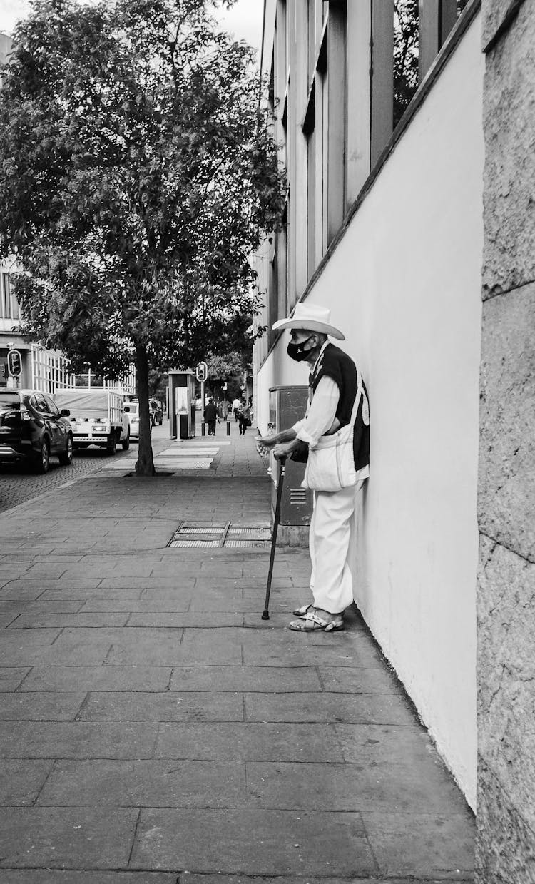 An Elderly Man With A Cane Standing On A Sidewalk