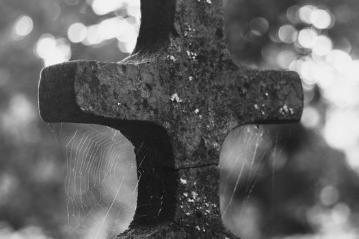 A rustic cross covered with spider webs captured in grayscale, evokes solitude and time's passage.