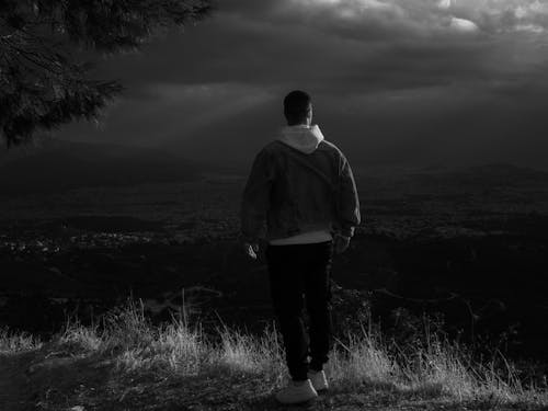 Grayscale Photo of a Person Standing at a Cliff