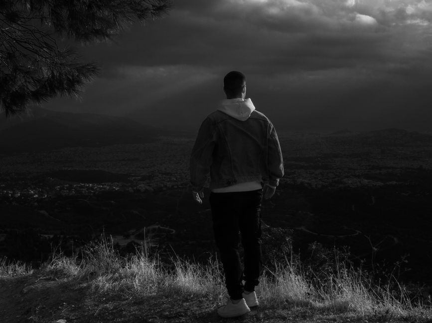 A lone man stands on a hill overlooking a vast landscape under a dramatic, cloudy sky.