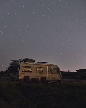 A serene night sky full of stars over a parked camper in a quiet wilderness setting.