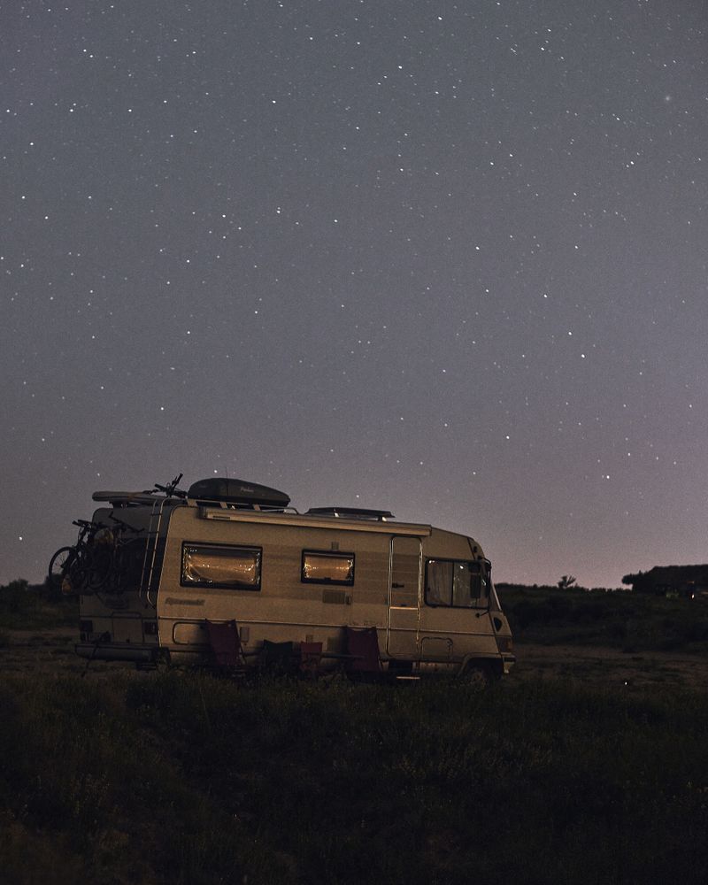 Autocaravana con las ventanas encendidas bajo un cielo estrellado