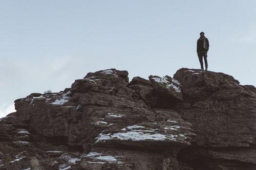 Free A man standing alone on a snowy rock outcrop under a clear sky, depicting solitude in nature. Stock Photo